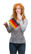 © Krakenimages.com - Young redhead woman holding flag of Germany cover mouth with hand shocked with shame for mistake, expression of fear, scared in silence, secret concept