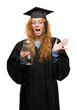 © Krakenimages.com - Young redhead student woman wearing graduated uniform holding hourglass very happy and excited, winner expression celebrating victory screaming with big smile and raised hands