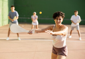 Wall Mural - Portrait of sporty young girl playing paleta fronton on outdoor court, ready to hit ball. Healthy and active lifestyle concept