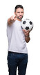© Krakenimages.com - Young man holding soccer football ball over isolated background pointing with finger to the camera and to you, hand sign, positive and confident gesture from the front