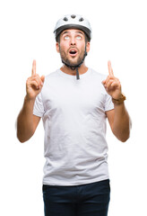 Sticker - Young handsome man wearing cyclist safety helmet over isolated background amazed and surprised looking up and pointing with fingers and raised arms.