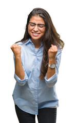 Wall Mural - Young beautiful arab woman wearing glasses over isolated background very happy and excited doing winner gesture with arms raised, smiling and screaming for success. Celebration concept.