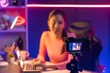 © Summit Art Creations - Smiling creative young beautiful Asian influencer recording on camera with positive podcast speech at night time, using laptop for presentation online at pink neon light modern studio. Stratagem.