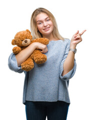 Wall Mural - Young caucasian woman holding cute teddy bear over isolated background very happy pointing with hand and finger to the side