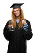 © Krakenimages.com - Young redhead student woman wearing graduated uniform holding hourglass happy with big smile doing ok sign, thumb up with fingers, excellent sign