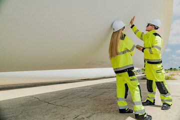 two engineers inspect a massive wind turbine blade at a construction site. the image showcases the s