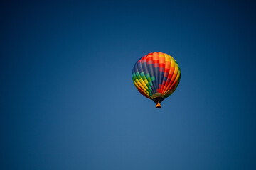 Colorful hot air balloon with red, green, yellow, purple, orange flying in blue sky with flame burning