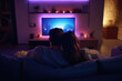 © Degimages - Young couple cuddling on sofa, watching a streaming show on smart TV, popcorn bowl nearby