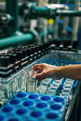 Technician collecting water samples at desalination plant, test tubes filled, complex filtration system background