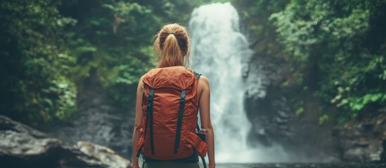 Wall Mural - woman with a backpack standing in front of a waterfall in the rainforest.