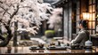© Vingar - A person enjoys a cup of tea and snacks while gazing at a cherry blossom tree in a tranquil Japanese garden.