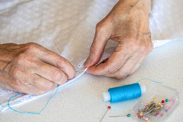 elderly female hands in the process of hand sewing, close-up, selective focus.