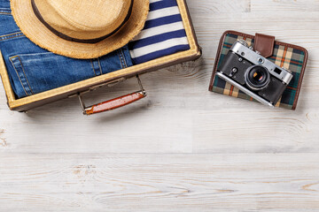 A travel bag with clothes, sun hat, flip flops, and a camera