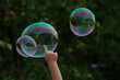 © Кристина Ненчева - A child plays with soap bubbles. A child's hand touches a soap bubble. There is a reflection of a building in the balloon.