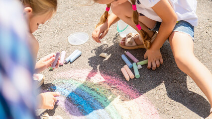 Sisters drawing rainbow with sidewalk chalk outside