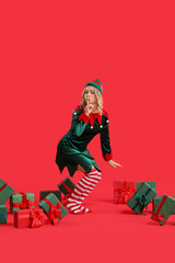 Poster - Beautiful young woman dressed as elf with Christmas gifts showing silence gesture on red background