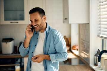 Wall Mural - Happy man having phone call over cell phone in  kitchen.