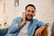 © Drazen - Smiling man listening music on headphones at home and looking at camera..