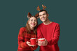 © Pixel-Shot - Beautiful young couple in reindeer horns holding cups of coffee with marshmallows on green background