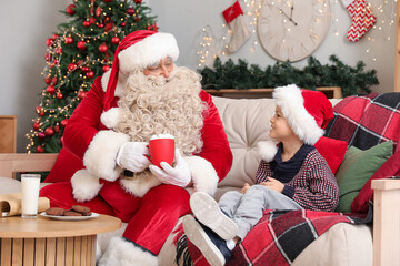 Wall Mural - Santa Claus and cute little boy drinking hot chocolate with marshmallows at home on Christmas eve