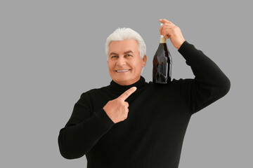 Wall Mural - Happy senior man with bottle of champagne celebrating Christmas on grey background