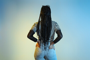 Cool young African-American woman with braids on color background, back view