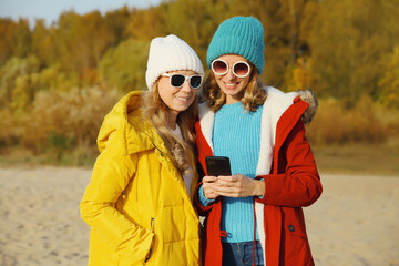 Wall Mural - Happy young women friends with smartphone together on beach, smiling girlfriends using phone on sea