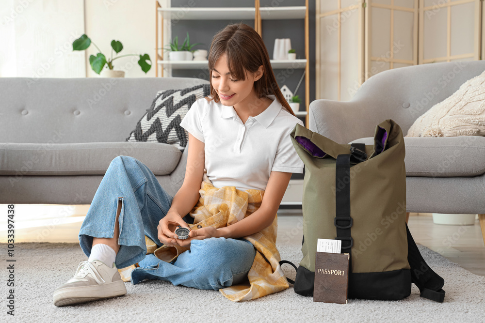 Female tourist with compass and backpack sitting on floor at home