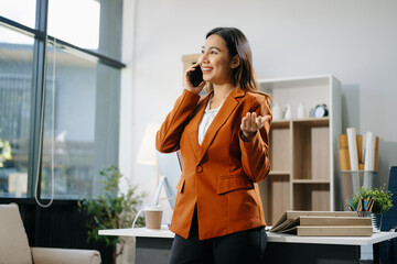 Smiling Asian woman talking on the phone with a customer Young positive female accountant using smartphone talking