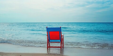 Poster - A red and blue beach chair by the sea, on the shore.