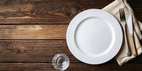 Aufkleber - An empty white plate with cutlery and a glass on a rustic wooden background. Flat lay, top view with copyspace.