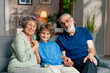 © Guys Who Shoot - a bright living room with sofa grandfather and grandmother sitting with grandson on sofa hugging looking at camera happy family