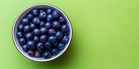 Aufkleber - Top view of small sour blue-black sloes in a bowl on a green background with copyspace.