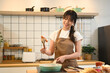 © Prathankarnpap - Smiling young asian woman preparing breakfast in a cozy kitchen