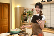 © Prathankarnpap - Smiling young woman standing in a kitchen, following a recipe or cooking tutorial online on digital tablet.