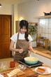 © Prathankarnpap - Happy young woman in apron preparing breakfast at home kitchen