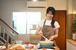 © Prathankarnpap - Happy young woman in apron preparing breakfast at home kitchen