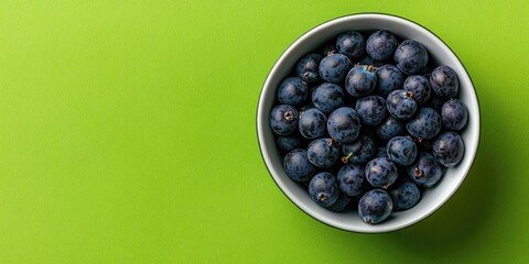 Aufkleber - Top view of small sour blue-black sloes in a bowl on a green background with copyspace.
