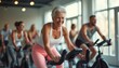 © natakot - An elderly woman smiling while working out on a stationary bike in a gym. The image highlights fitness, health, and active lifestyle for seniors.