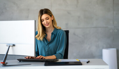 Young happy successful business woman working with computer in corporate office