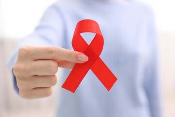 Wall Mural - Woman with red ribbon on light background, closeup. HIV (AIDS) disease awareness