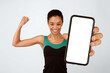 © Prostock-studio - Body Shaping Apps. Sporty Afro Woman Holding Phone With Blank Screen Showing Biceps Standing Over Yellow Background. Mockup, Studio Shot