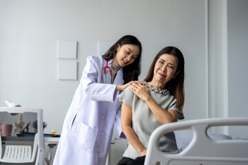 Doctor examining mature patient suffering from shoulder pain in hospital room