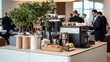 © Sansern - Modern office break room with coffee machine, pastries, and a small plant.  Men in suits stand around the counter.