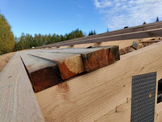 A close-up of cut lumber pieces stacked on a construction site with a view of the open sky and surrounding trees in the background