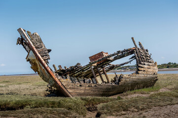 Abandoned old wooden fishing boat by river with grass and blue sky in background, shipwreck, ships graveyard, Wyre, Fleetwood