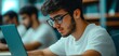 © Theraphol - Young male student working on laptop in a library, focused and concentrated.
