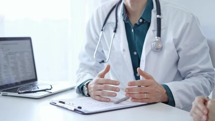 Wall Mural - Doctor and a patient. The physician, wearing a white medical coat over a green shirt, gesturing with his hands during a consultation in the clinic. Medical service