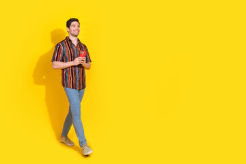 Wall Mural - Full length portrait of nice young man phone walk empty space wear shirt isolated on yellow color background