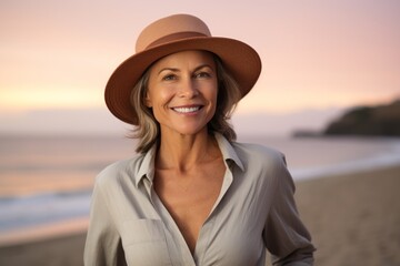 Canvas Print - Portrait of a cheerful woman in her 50s donning a classic fedora in stunning sunset beach background